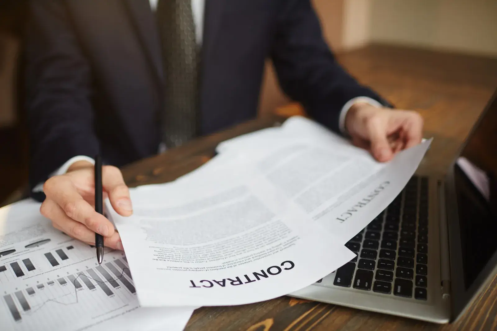 A man in a suit holding contract pages over printed financial charts