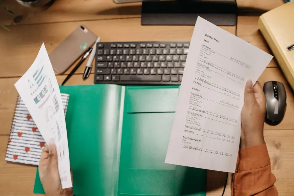 Hands reviewing a balance sheet and financial charts at a desk